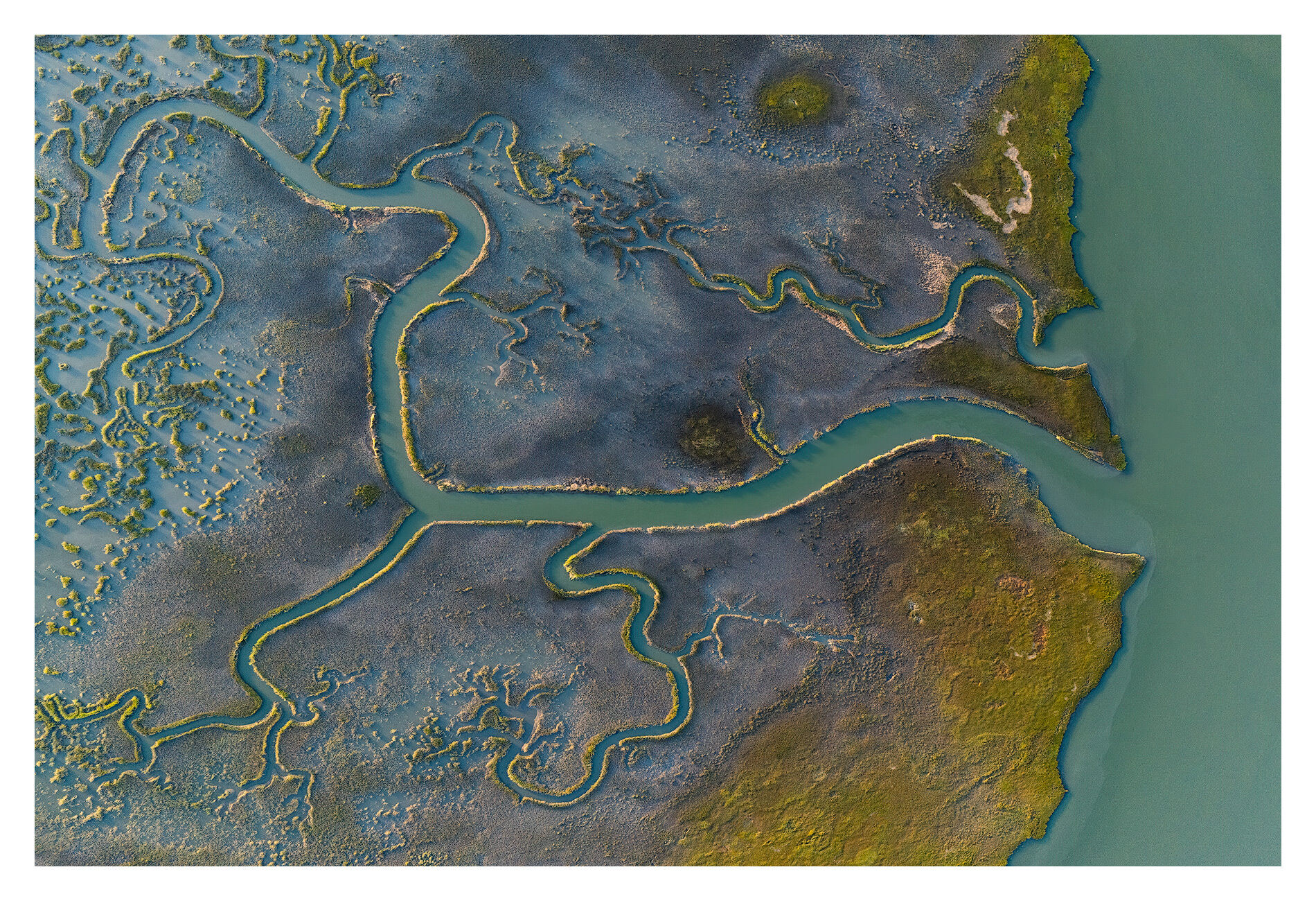Meandering tidal streams interlace across the marsh, forming intricate patterns that shift with each rise and fall of the tide...